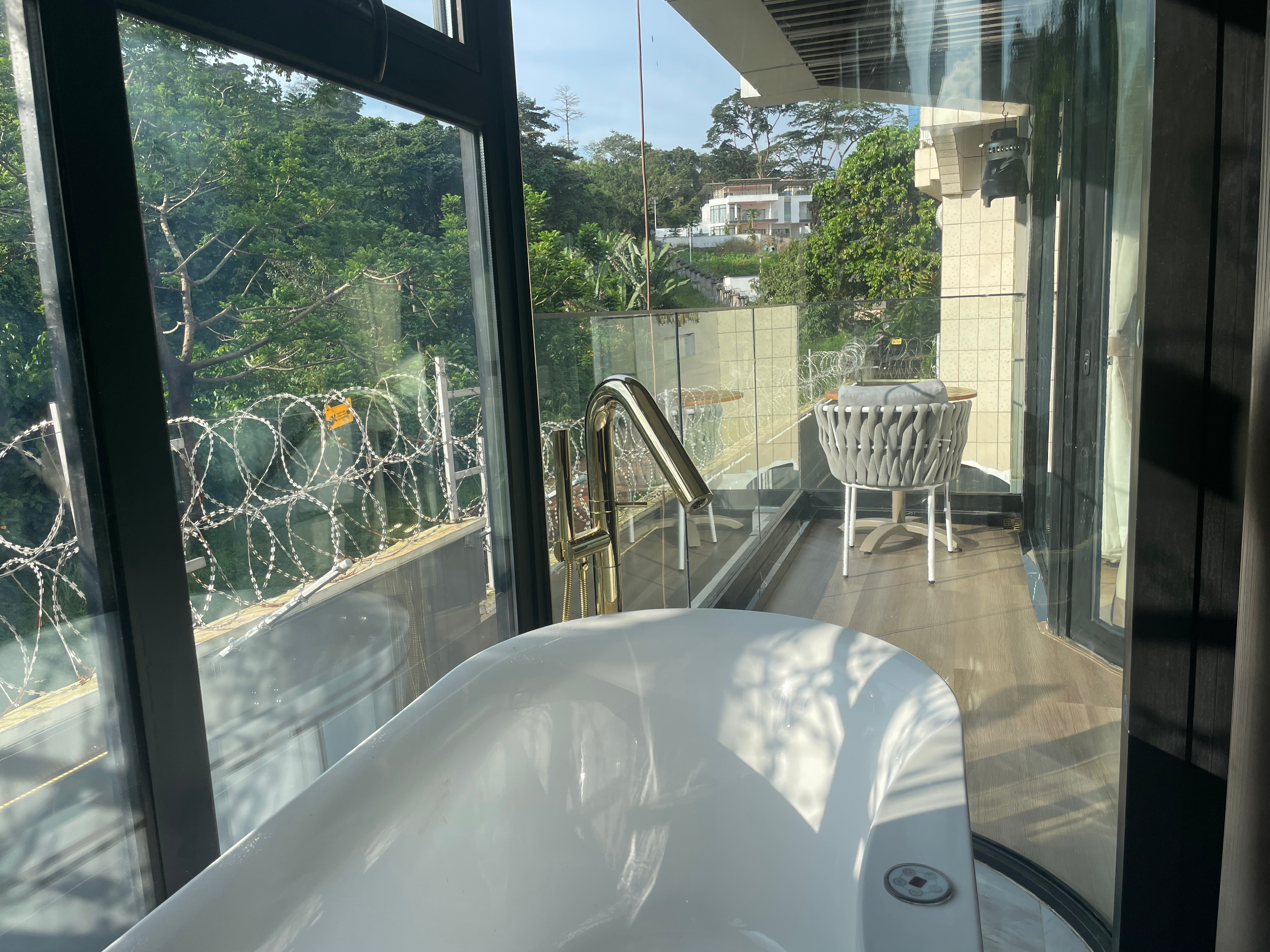 Freestanding bathtub with gold trim and forest view through balcony